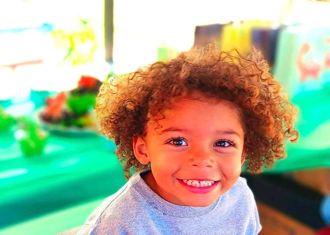 Eli is registered to the contest to win money with this photo: afro, child, chin, event, facial_expression, fun, hairstyle, happy, jheri_curl, joy, laugh, leisure, magenta, person, portrait_photography, recreation, ringlet, skin, smile, toddler