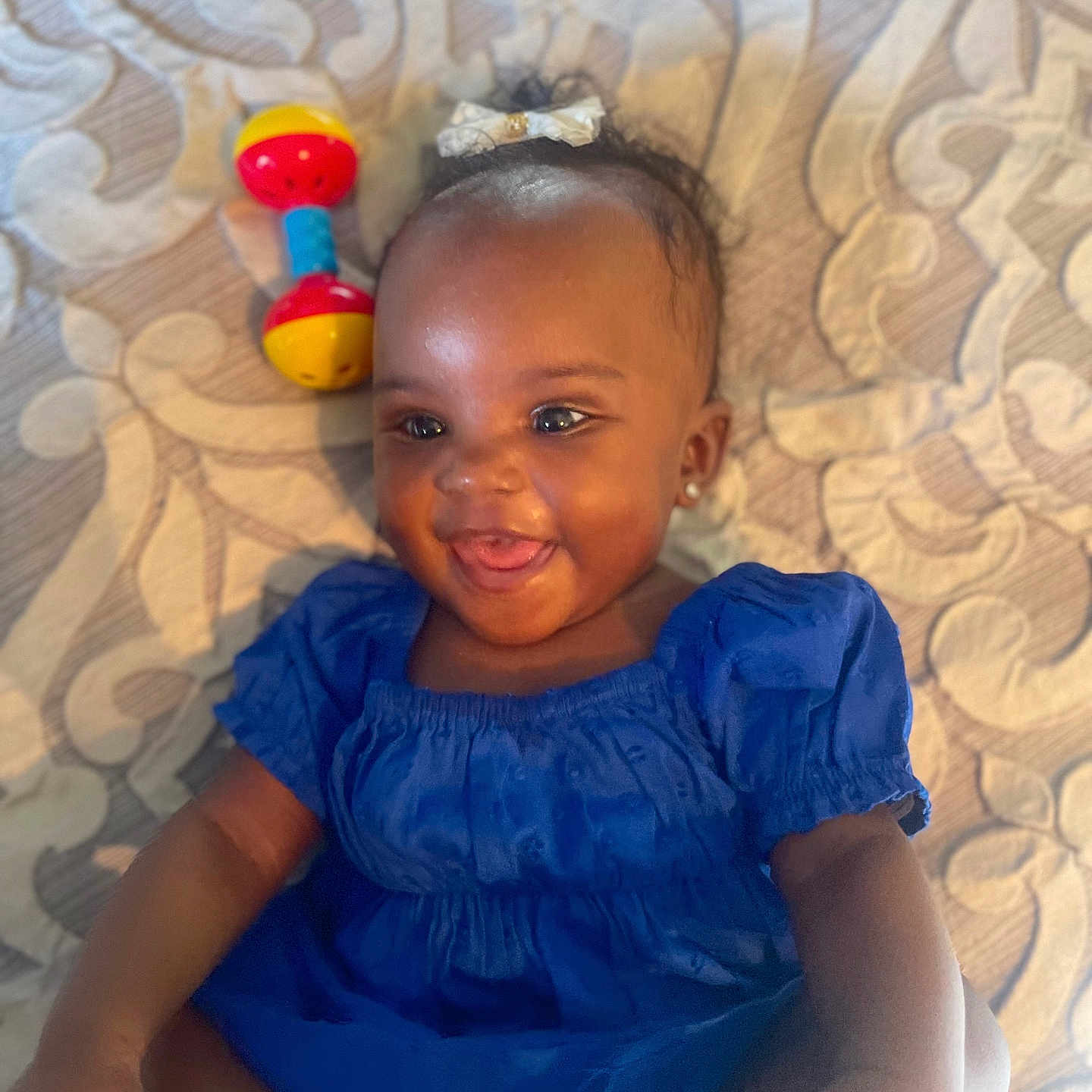 Kaija is registered to the contest to win money with this photo: baby, blue_dress, bow, child, closeup, cute, earrings, foot, hand, happy, indoors, infant, lying_down, patterned_quilt, person, portrait, rattle, skin, smiling, toy