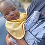 Kaija is registered to the contest to win money with this photo: baby, smile, yellow_bib, infant, happy, person, arm, clothing, holding, portrait, outdoor, blurred_background, casual_wear, skin, head, face, joy, child, closeup, expression