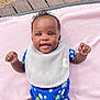 baby, smiling, blue_onesie, daisies, bees, pink_blanket, outdoor, grass, wooden_deck, earrings, happy, infant, cute, lying_down, child, person, face, hand, skin, portrait