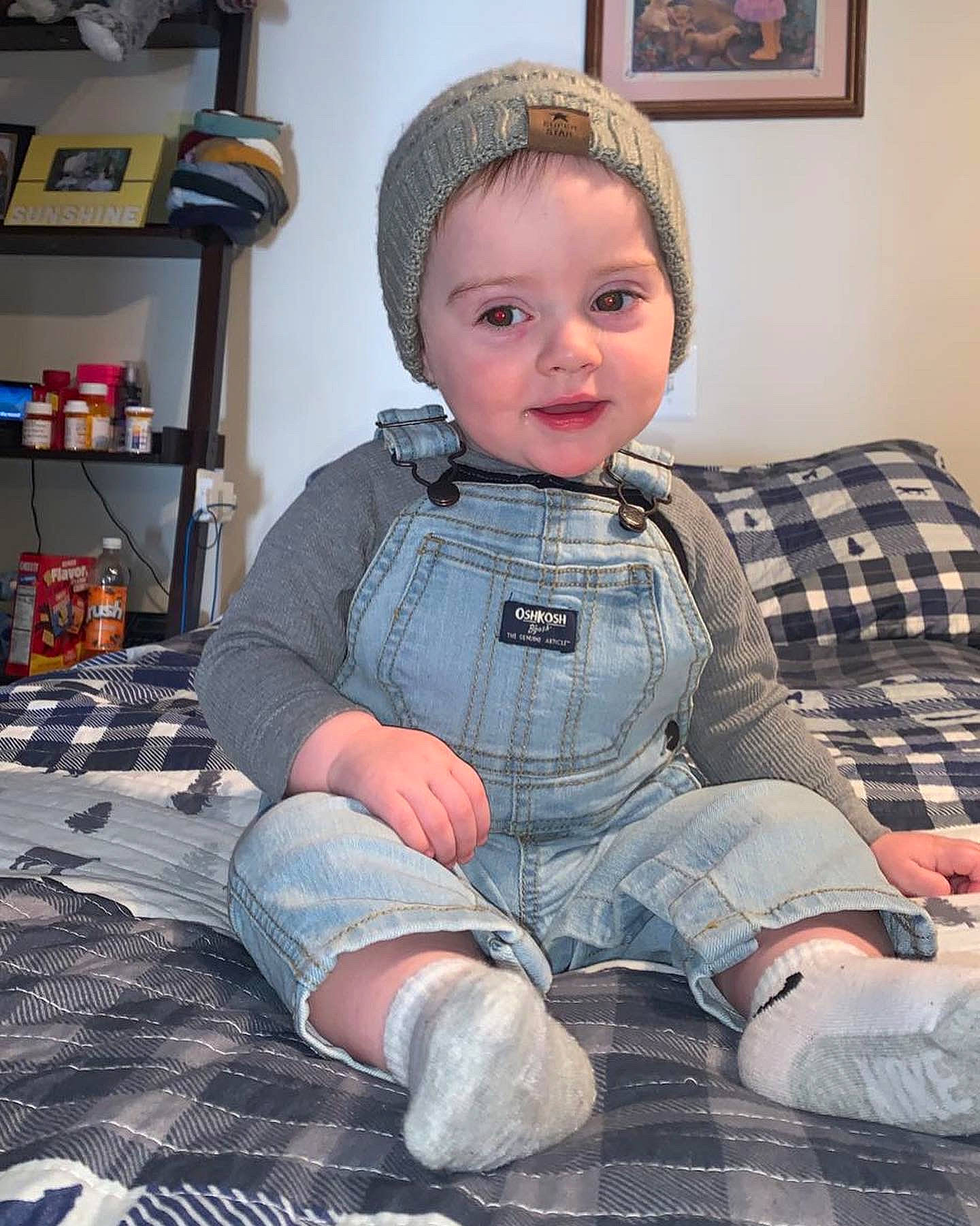 Landon is registered to the contest to win money with this photo: baby_toddler_clothing, cheek, comfort, eye, facial_expression, floor, flooring, head, headwear, human_body, leg, mouth, person, picture_frame, shelf, skin, sleeve, standing, textile, thigh