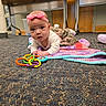 baby, headband, pink_bow, blanket, crocheted, carpet, toy_rings, floor, indoor, table, wooden, curious, child, infant, clothing, white_shirt, camouflage_skirt, person, playtime, crawling
