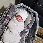 Ayaan is registered to the contest to win money with this photo: baby, baby_carrier, blanket, carpet, child, comfortable, cozy, floor, gray_blanket, hat, indoor, infant, leather_couch, newborn, peaceful, portrait, resting, sleeping, soft, swaddled