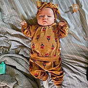 Lilly is registered to the contest to win money with this photo: baby, infant, clothing, headwear, bed, blanket, pacifier, socks, pattern, face, person, lying_down, indoor, striped, fabric, soft, cute, child, expression, cozy