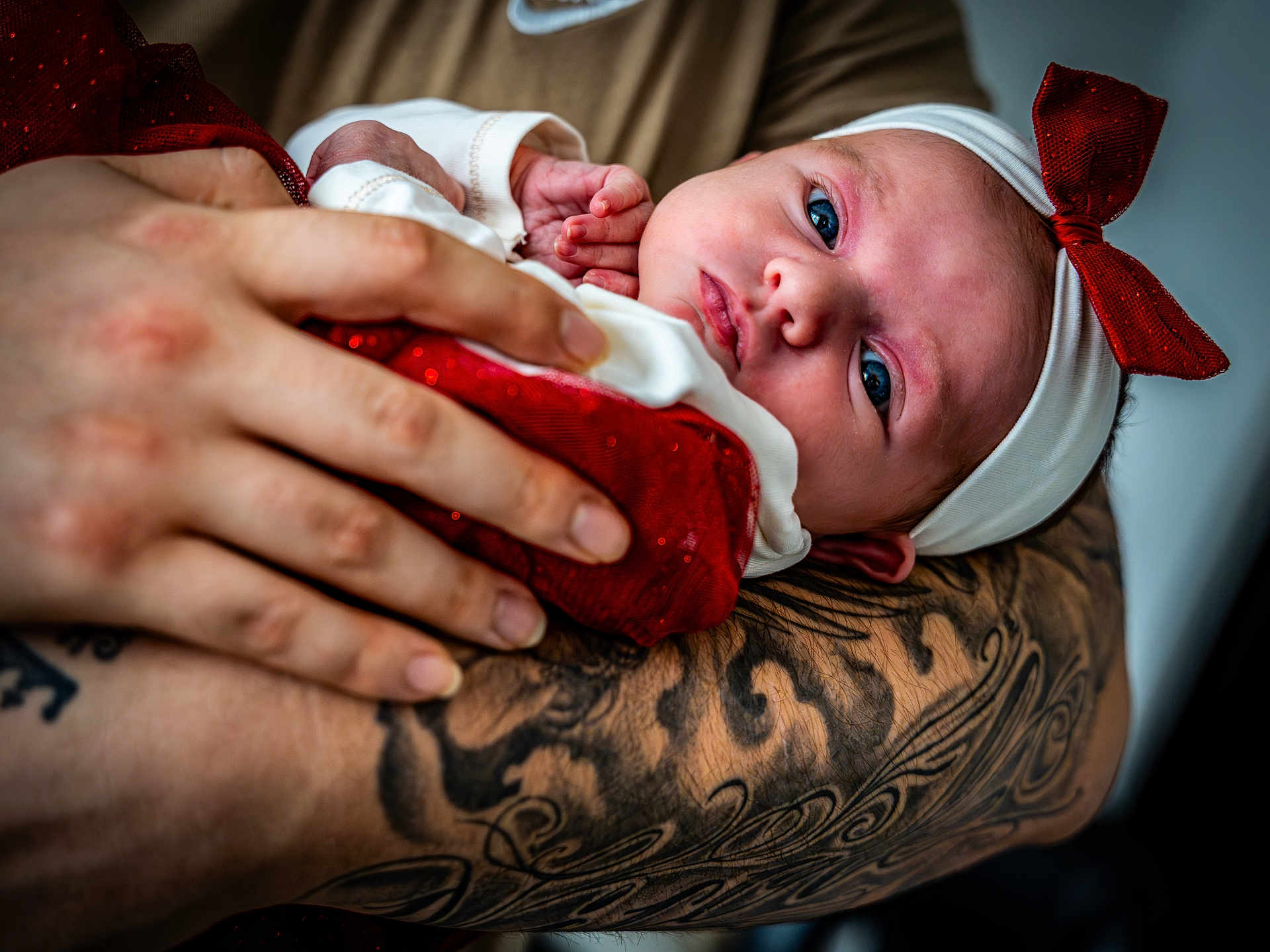 Eliana participe au concours pour gagner de l'argent avec cette photo : baby, newborn, infant, child, person, face, blue_eyes, headband, bow, red_clothing, white_clothing, tattoo, arm, hand, skin, close_up, portrait, holding, gentle, indoor