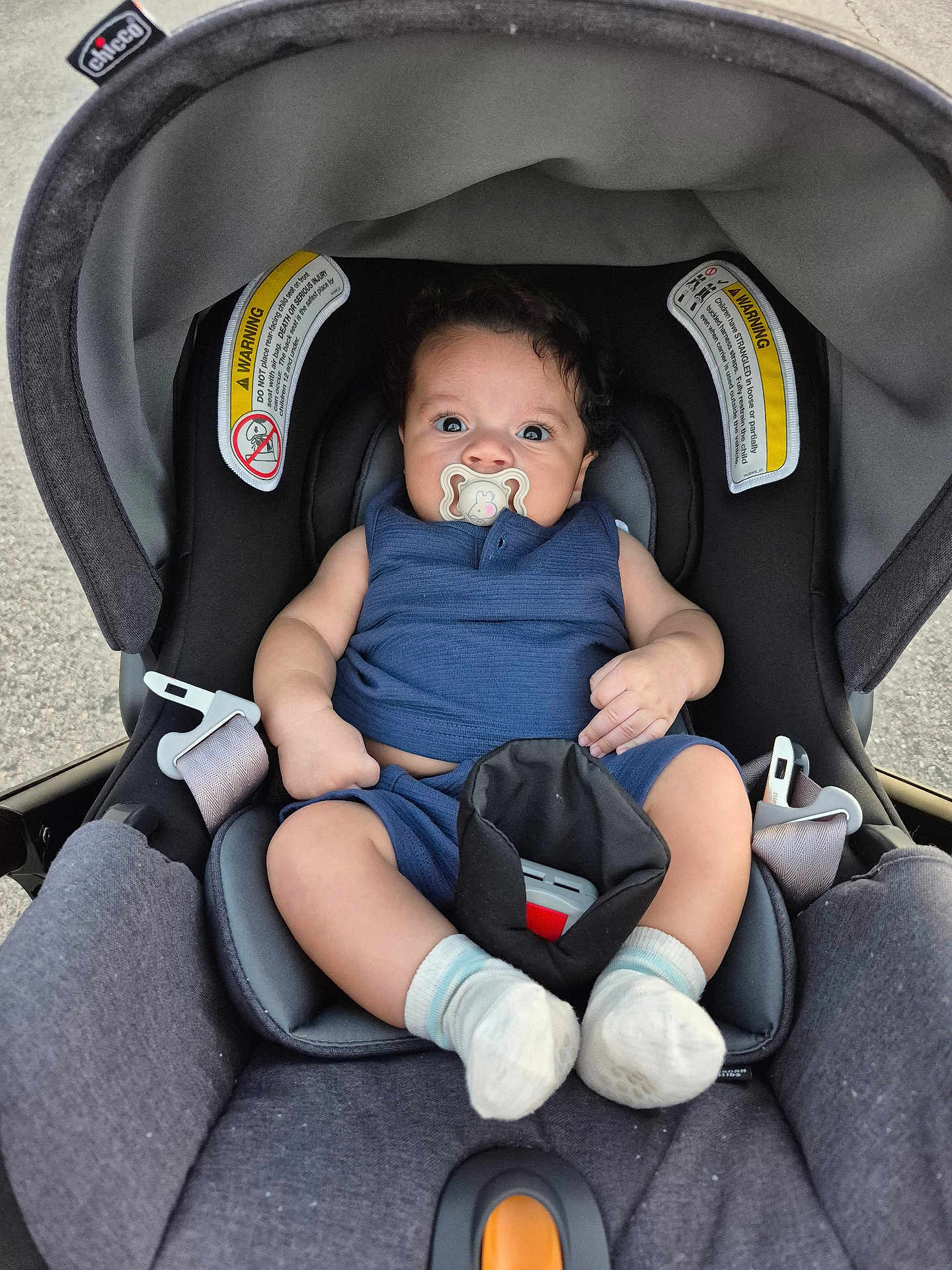 Miller James is registered to the contest to win money with this photo: baby, pacifier, car_seat, blue_outfit, socks, curly_hair, infant, child, seatbelt, sitting, indoors, closeup, cute, young_child, person, portrait, chicco, comfortable, wide_eyes, car
