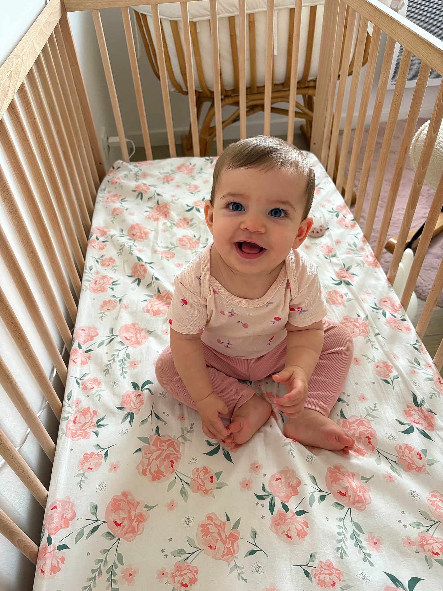 Gabriela participe au concours pour gagner de l'argent avec cette photo : baby, child, crib, wooden_crib, floral_bedding, pink_clothing, smiling, sitting, indoors, cute, happy, person, infant, blue_eyes, soft_lighting, room, floor, chair, foot, hand