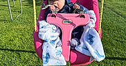 Liam joined the competition — help win amazing prizes! baby, child, swing, pink_swing, blanket, blue_hat, blue_jacket, outdoor, grass, trampoline, sunny, daylight, hill, chewing, strap, playground, seat, young_child, nature, fun