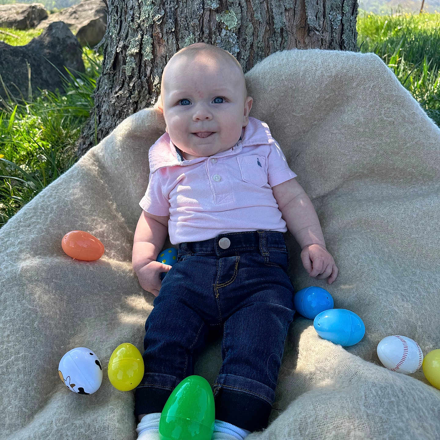 Liam is registered to the contest to win money with this photo: baby, child, outdoor, tree, blanket, easter_eggs, grass, mountains, blue_sky, clothing, jeans, polo_shirt, socks, smile, face, nature, sunlight, playful, seasonal, spring