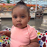 Tru is registered to the contest to win money with this photo: baby, child, shopping_cart, supermarket, polka_dot, clothing, pink_shirt, curly_hair, earrings, seat_belt, aisle, shelf, store, indoor, person, portrait, face, expression, shopping, retail