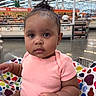 baby, child, shopping_cart, supermarket, polka_dot, clothing, pink_shirt, curly_hair, earrings, seat_belt, aisle, shelf, store, indoor, person, portrait, face, expression, shopping, retail