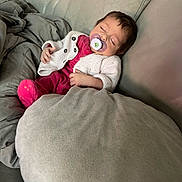 Inaya a rejoint le concours — aidez-le/la à gagner de superbes lots ! baby, sleeping, pacifier, couch, blanket, pillow, knitted_sweater, pink_clothing, infant, indoor, resting, child, comfort, soft_fabric, relaxation, peaceful, cozy, young_child, face, person