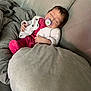 baby, sleeping, pacifier, couch, blanket, pillow, knitted_sweater, pink_clothing, infant, indoor, resting, child, comfort, soft_fabric, relaxation, peaceful, cozy, young_child, face, person