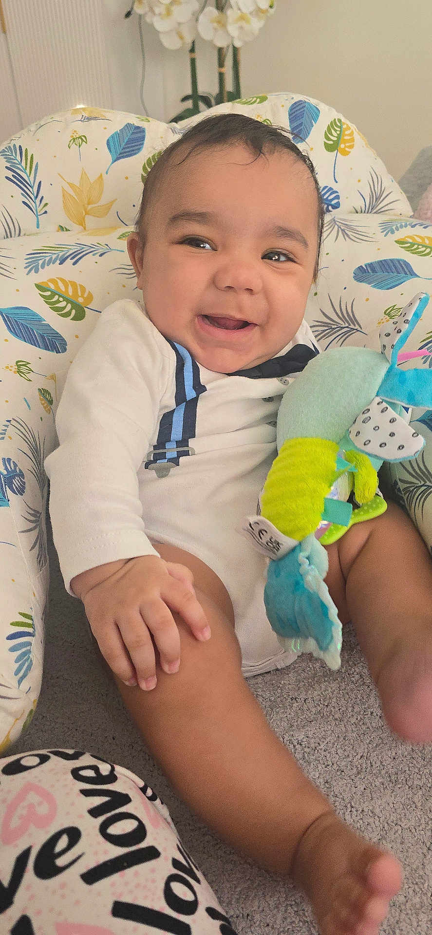 Sebastian joined the competition — help win amazing prizes! baby, smiling, infant, plush_toy, cushion, leaf_pattern, indoor, carpet, white_outfit, blue_suspenders, hand, foot, face, happy, child, cute, seated, home, decor, flower