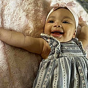 Isabella joined the competition — help win amazing prizes! baby, smiling, headband, dress, infant, happy, cute, child, portrait, lying_down, skin, face, arm, blanket, textile, patterned_clothing, indoors, closeup, person, cheerful