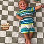 baby, child, smiling, striped_clothing, plush_blanket, checkered_pattern, wooden_plaques, infant, happy, lying_down, cute, portrait, indoors, feet, arms, head, person, colorful, playful, young