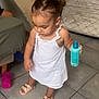 Marie a rejoint le concours — aidez-le/la à gagner de superbes lots ! bottle, casual, child, floor, footwear, furniture, hair, holding_object, indoors, looking_down, person, pigtails, pink_cup, sandals, standing, tile, toddler, wall, white_dress, young_child