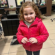 Alia a rejoint le concours — aidez-le/la à gagner de superbes lots ! bright_lighting, casual_clothing, chair, child, curly_hair, floor_tiles, girl, hair, hands, happy, indoor, mirror, person, portrait, red_jacket, reflection, salon, smile, standing, young
