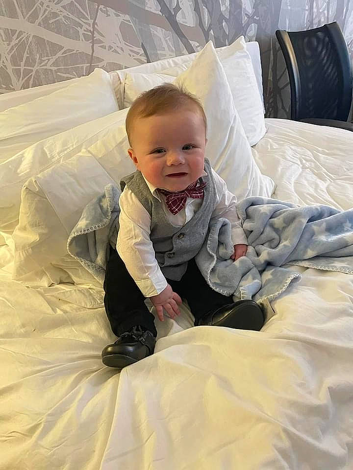 Jameson is registered to the contest to win money with this photo: baby, baby_toddler_clothing, bedding, child, comfort, facial_expression, floor, flooring, fun, hairstyle, happy, head, jacket, linens, person, product, sitting, sleeve, smile, textile