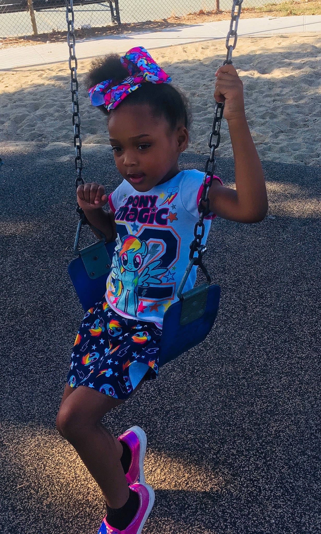 Jasaiah is registered to the contest to win money with this photo: arm, black, child, city, cool, electric_blue, face, facial_expression, fun, happy, leisure, person, pink, playground, product, sleeve, standing, summer, swing, t_shirt