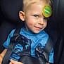 child, car_seat, seat_belt, blue_shirt, blonde_hair, stickers, smile, young_child, safety, portrait, indoor, cute, face, person, casual, happy, childhood, car_interior, close_up, playful