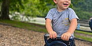 Logan is registered to the contest to win money with this photo: blue_shoes, casual_clothing, child, daylight, fun, greenery, happy, nature, outdoor, pants, park, person, playground, playtime, seesaw, short_sleeves, smiling, tree, woodchips, young_child