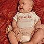baby, child, chubby_legs, clothing, cozy, cute, happy, indoor, infant, looking_away, onesie, person, portrait, red_blanket, sitting, skin, smile, soft, texture, young