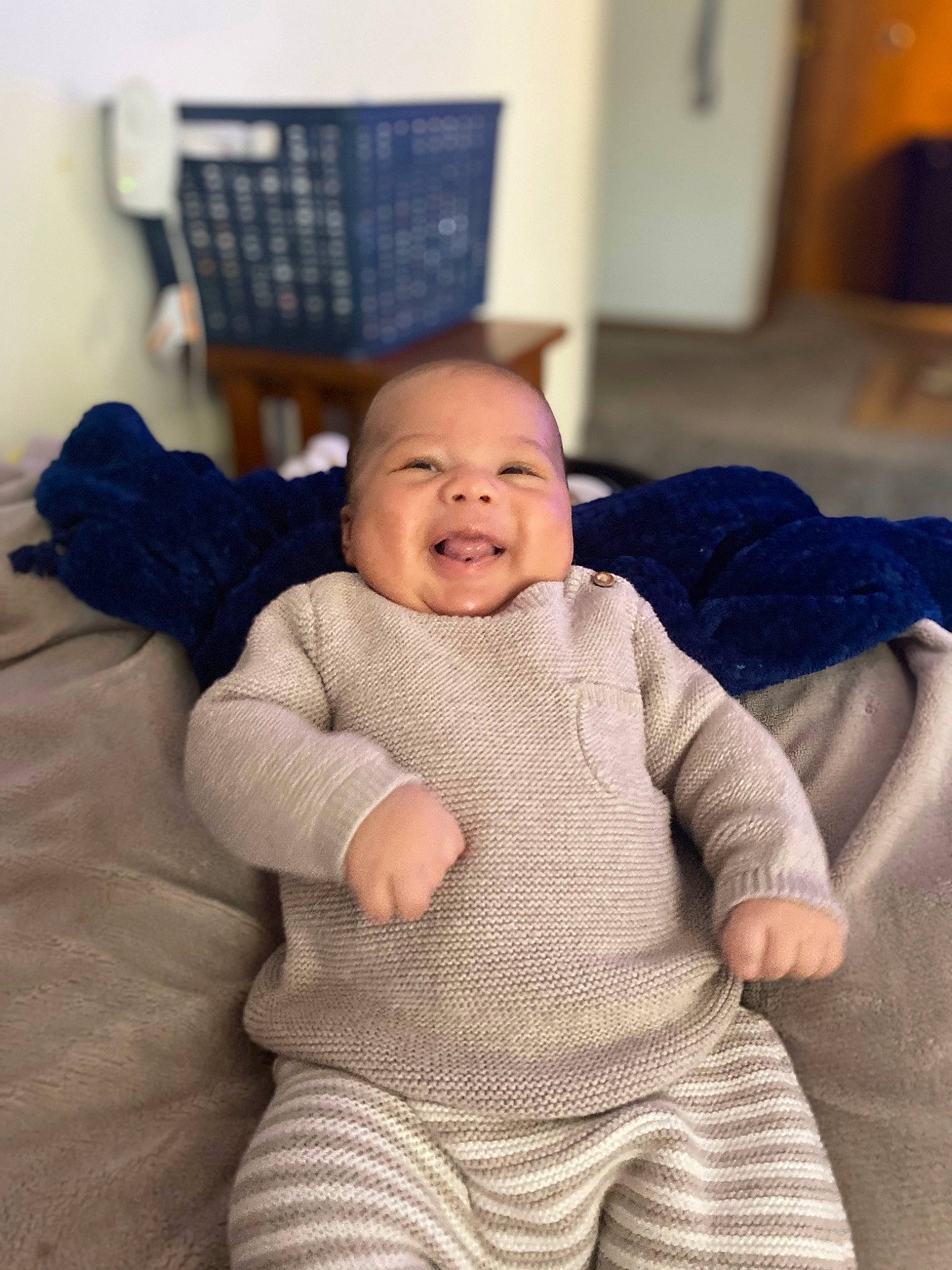 Jakobe is registered to the contest to win money with this photo: baby, baby_toddler_clothing, cheek, child, comfort, couch, eye, flooring, fur, happy, laugh, linens, person, room, sitting, skin, sleeve, smile, toddler, wood