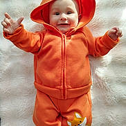 Valentin participe au concours pour gagner de l'argent avec cette photo : apparel, baby, blanket, child, cute, expression, face, fox_hood, hands, happy, hoodie, indoors, infant, lying_down, orange_clothing, pants, person, playful, smiling, soft_texture