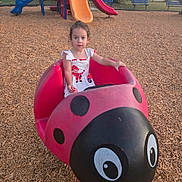 Lilith is registered to the contest to win money with this photo: child, toddler, girl, playground, ladybug_ride, outdoor, park, slide, play_equipment, sitting, portrait, wide_eyed, dress, pink, white, wood_chips, summer, recreation, colorful, daylight