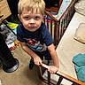 child, boy, blonde_hair, blue_shirt, bed, bedroom, car_toys, carpet, laundry_basket, pillow, blanket, wooden_rail, fan, furniture, indoor, person, toy, clothing, floor, looking_up