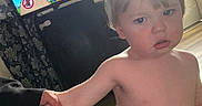 Wesley is registered to the contest to win money with this photo: adult_hand, blond_hair, cartoon, child, curtains, daylight, expression, face, furniture, hand_holding, home, indoor, living_room, person, shirtless, television, toddler, window, wooden_floor, young_child