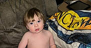 Wesley joined the competition — help win amazing prizes! toddler, child, shirtless, shorts, brown_chair, blanket, indoor, furniture, curious_expression, person, face, hair, skin, seated, living_room, box, tablet, wood_panel_wall, red_surface, casual