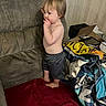Wesley is registered to the contest to win money with this photo: toddler, child, barefoot, shorts, blanket, couch, indoor, furniture, person, baby, skin, face, hair, room, box, pile, standing, red, gray, curly_hair