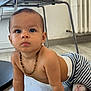 baby, child, crawling, floor, striped_pants, necklace, indoor, modern_chair, wooden_floor, curious, person, furniture, beads, young_child, candid, flooring, expression, head, hands, home