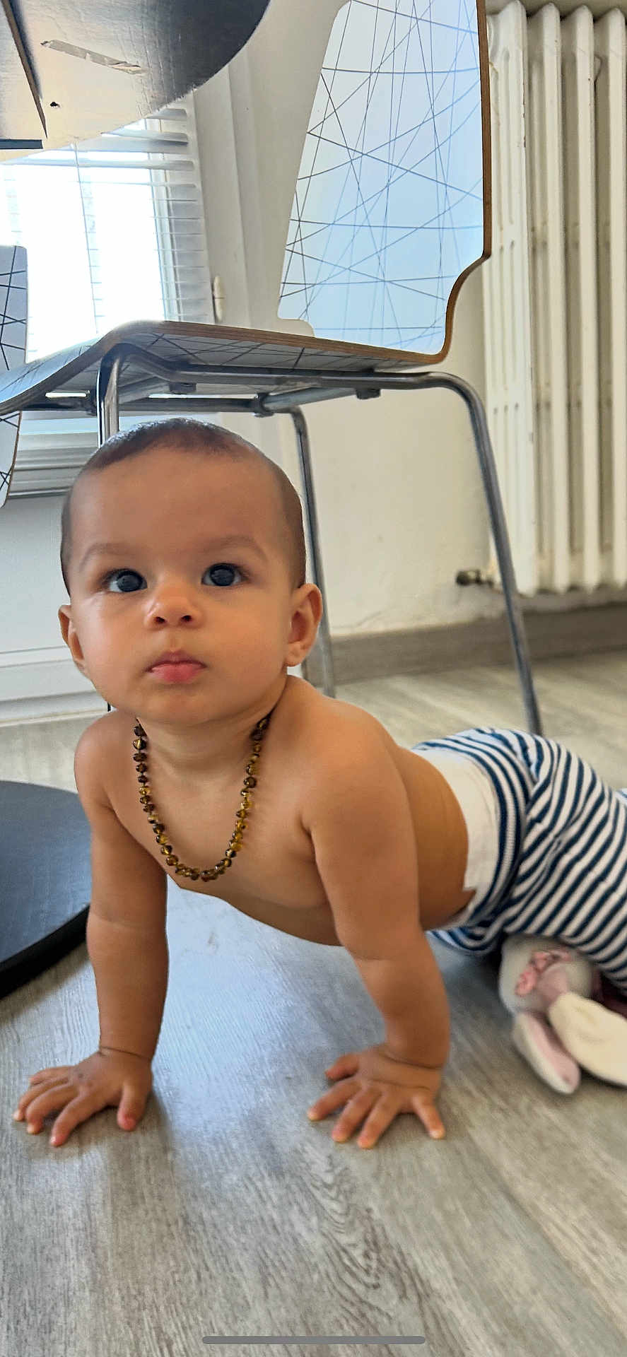 Adèle participe au concours pour gagner de l'argent avec cette photo : baby, child, crawling, floor, striped_pants, necklace, indoor, modern_chair, wooden_floor, curious, person, furniture, beads, young_child, candid, flooring, expression, head, hands, home