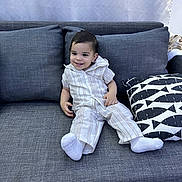 Aiden is registered to the contest to win money with this photo: toddler, child, smiling, couch, gray_couch, pillow, striped_outfit, white_socks, indoor, living_room, happy, relaxed, modern_furniture, fabric_texture, head, person, seated, home, casual, cute