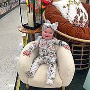 Claire joined the competition — help win amazing prizes! aisle, armchair, baby, carpet, child, cute, decorative_pillow, floor, floral_clothing, happy, headband, indoor, lantern, person, pinwheel, rattan_chair, seated, smile, store, wooden_table