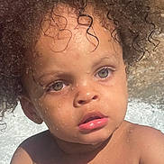 Sulieman joined the competition — help win amazing prizes! child, toddler, curly_hair, wet_skin, water_droplets, blue_object, outdoor, sunlight, face, eyes, hands, playing, summer, skin, portrait, expression, closeup, baby, person, nature