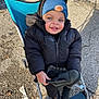 Sulieman is registered to the contest to win money with this photo: toddler, child, stroller, black_jacket, blue_beanie, football_patch, boots, outdoor, sunlight, smile, concrete, leaves, winter_clothing, footwear, person, young_child, casual, daylight, happy, curious