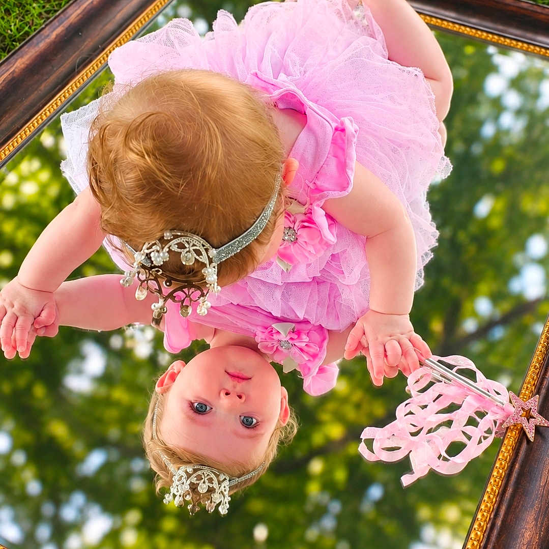 Alexis is registered to the contest to win money with this photo: baby, child, infant, pink_dress, dress, headpiece, tiara, jewelry, mirror, reflection, upside_down, outdoor, grass, trees, bokeh, portrait, fashion, frills, ornate_frame, photography