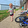 barefoot, bicycle, bike, blue_sky, brick_wall, chair, child, curly_hair, daytime, flowers, grass, house, outdoor, play, power_lines, shorts, sidewalk, summer, toddler, tshirt