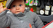 Thaïs a rejoint le concours — aidez-le/la à gagner de superbes lots ! baby, child, shopping_cart, hat, grey_sweater, store, grocery_store, bottles, beverages, shelves, curious, face, person, indoor, retail, shopping, cute, infant, cap, hand_raised