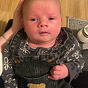 Teagan is registered to the contest to win money with this photo: baby, child, infant, overalls, denim, floral_clothing, hand, floor, wooden_floor, portrait, closeup, cute, newborn, person, indoor, warm_lighting, skin, face, eyes, expression