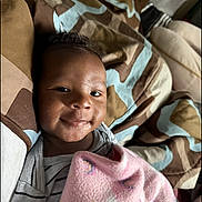 Noah is registered to the contest to win money with this photo: baby, blanket, bedspread, smile, infant, striped_clothing, face, indoors, child, comfort, patterned, fabric, person, cute, lying_down, soft_light, happy, young_child, cozy, portrait