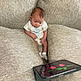 baby, infant, couch, tablet, screen, flowers, sitting, curious, indoors, clothing, socks, technology, furniture, child, young, device, comfortable, home, reflection, soft