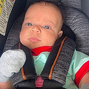Brooks is registered to the contest to win money with this photo: baby, infant, car_seat, seatbelt, blanket, football_pattern, star_pattern, mittens, clothing, child, face, head, person, sitting, closeup, cute, indoors, safety, transport, newborn