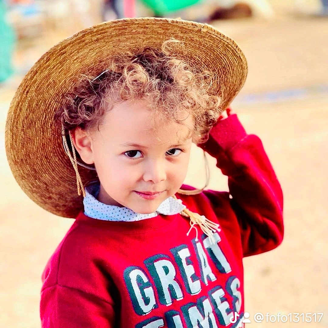 Rakan is registered to the contest to win money with this photo: casual_wear, child, childhood, curly_hair, cute, daylight, face, fashion, fun, happy, headwear, looking_at_camera, outdoor, person, playful, portrait, red_sweater, smiling, straw_hat, young