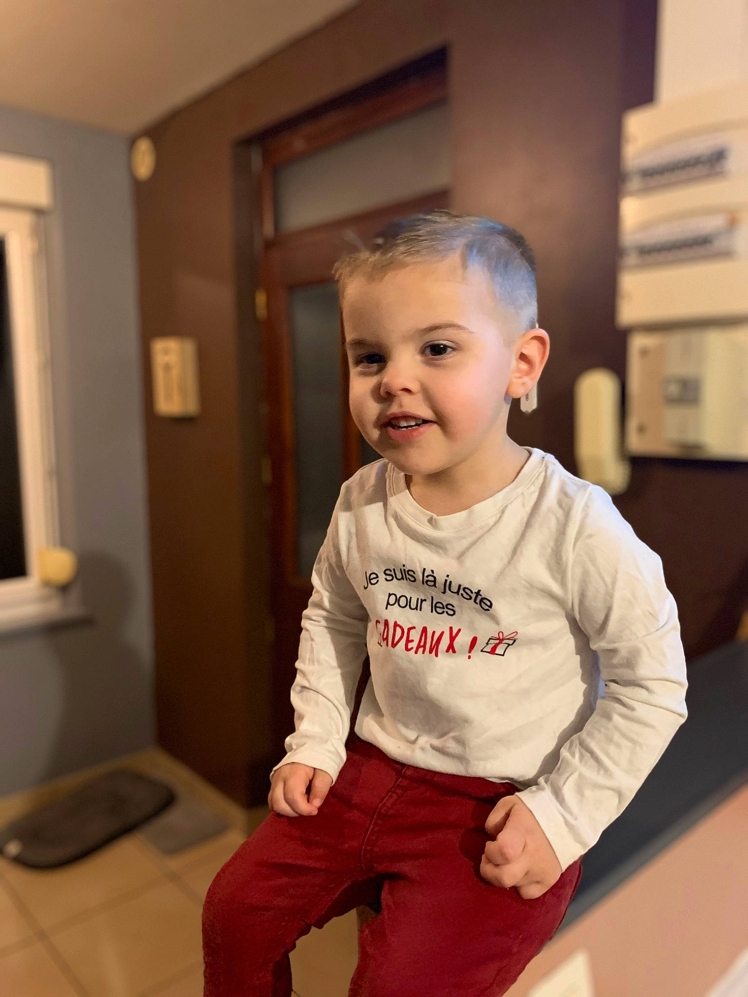 Charly participe au concours pour gagner de l'argent avec cette photo : baby, baby_toddler_clothing, cheek, child, comfort, door, floor, flooring, happy, hardwood, joy, knee, person, picture_frame, room, sitting, sleeve, smile, standing, t_shirt