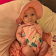 Adeline joined the competition — help win amazing prizes! baby, infant, pink_hat, floral_swimsuit, bow, blanket, soft_fabric, couch, indoors, cute, chubby_arms, chubby_legs, sitting, face, headwear, summer_clothing, child, person, portrait, skin